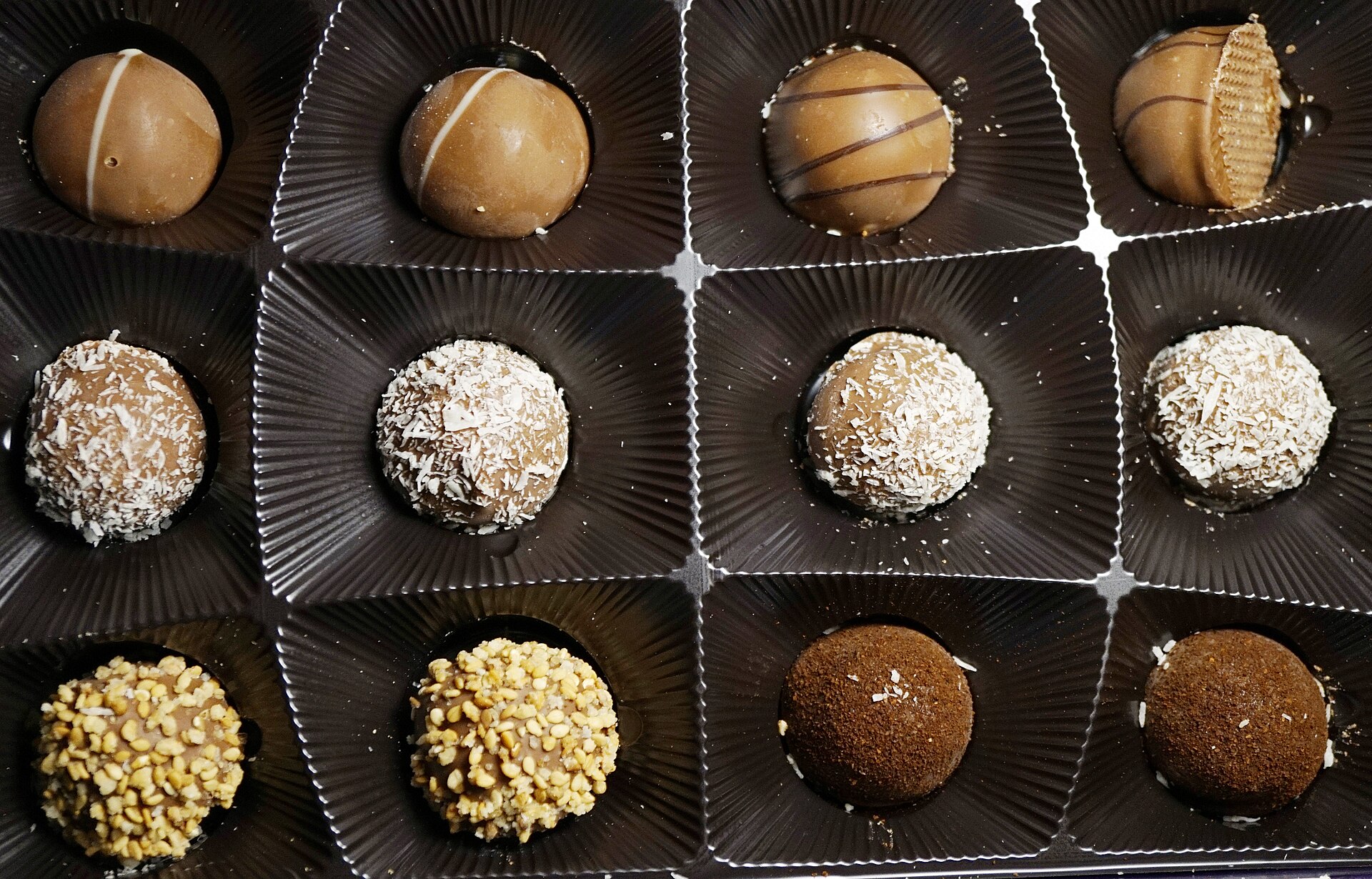 Caixa com trufas e docinhos sortidos em forminhas escuras.